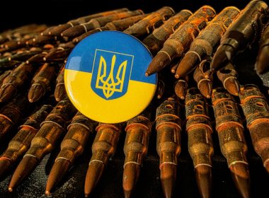 a blue and yellow button sitting on top of a pile of bullet shells
