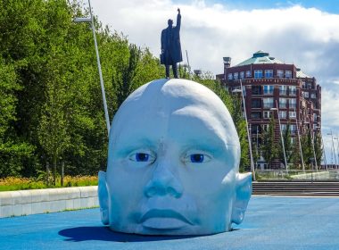 Giant blue head sculpture with a man on top