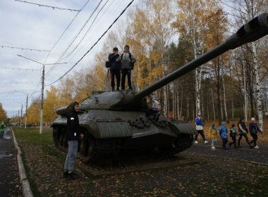 People stand on and around a military tank outdoors.